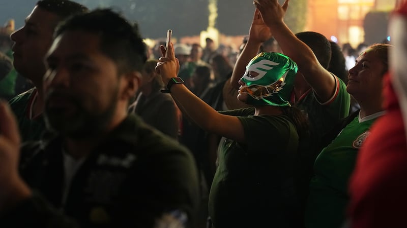 Gente observa a la presidenta de México, Claudia Sheinbaum, dar el grito anual desde el balcón...